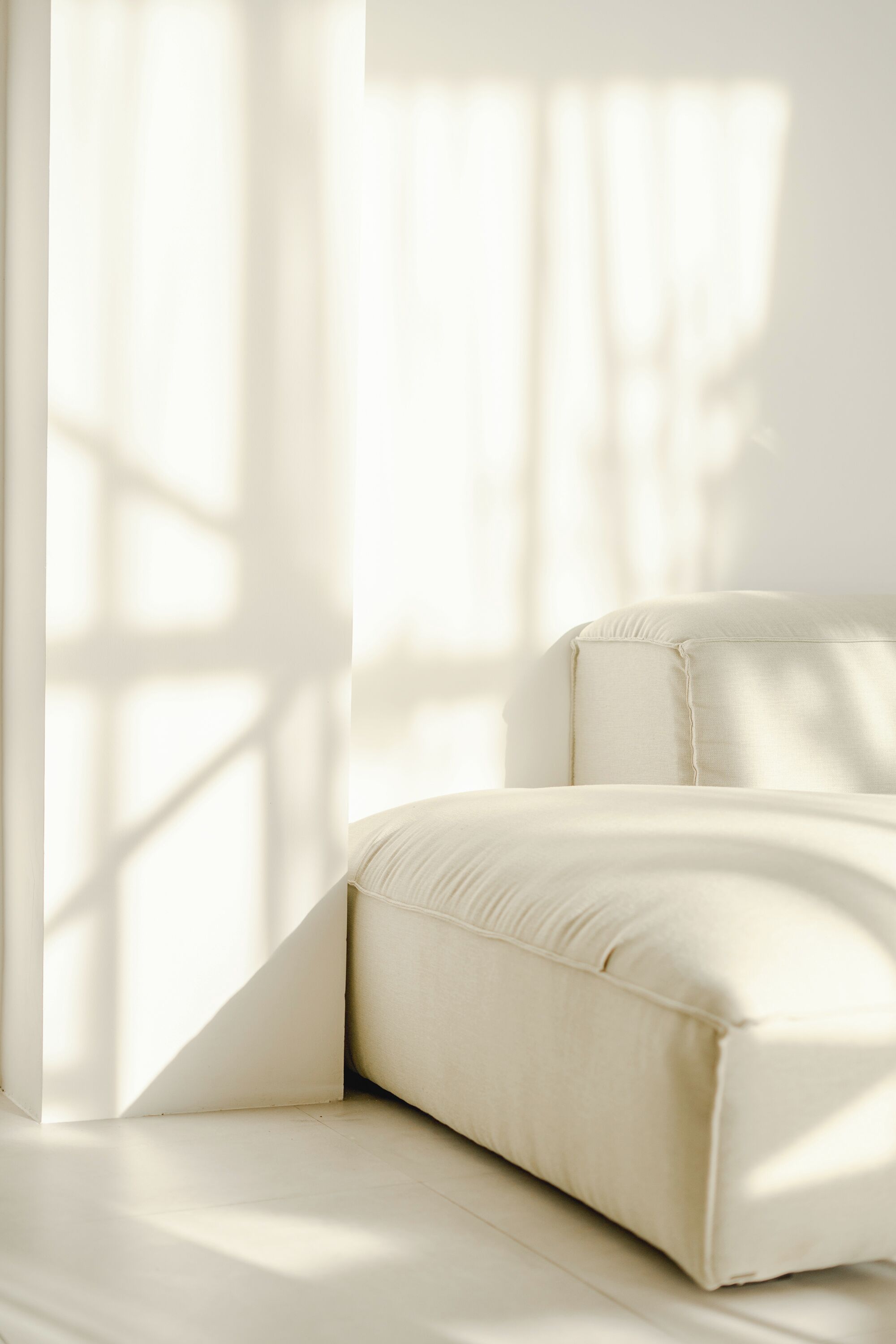 A minimalist room with a white sofa and a large window casting shadows.