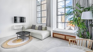 A modern living room with a sofa, a coffee table, a TV, and large windows with curtains.