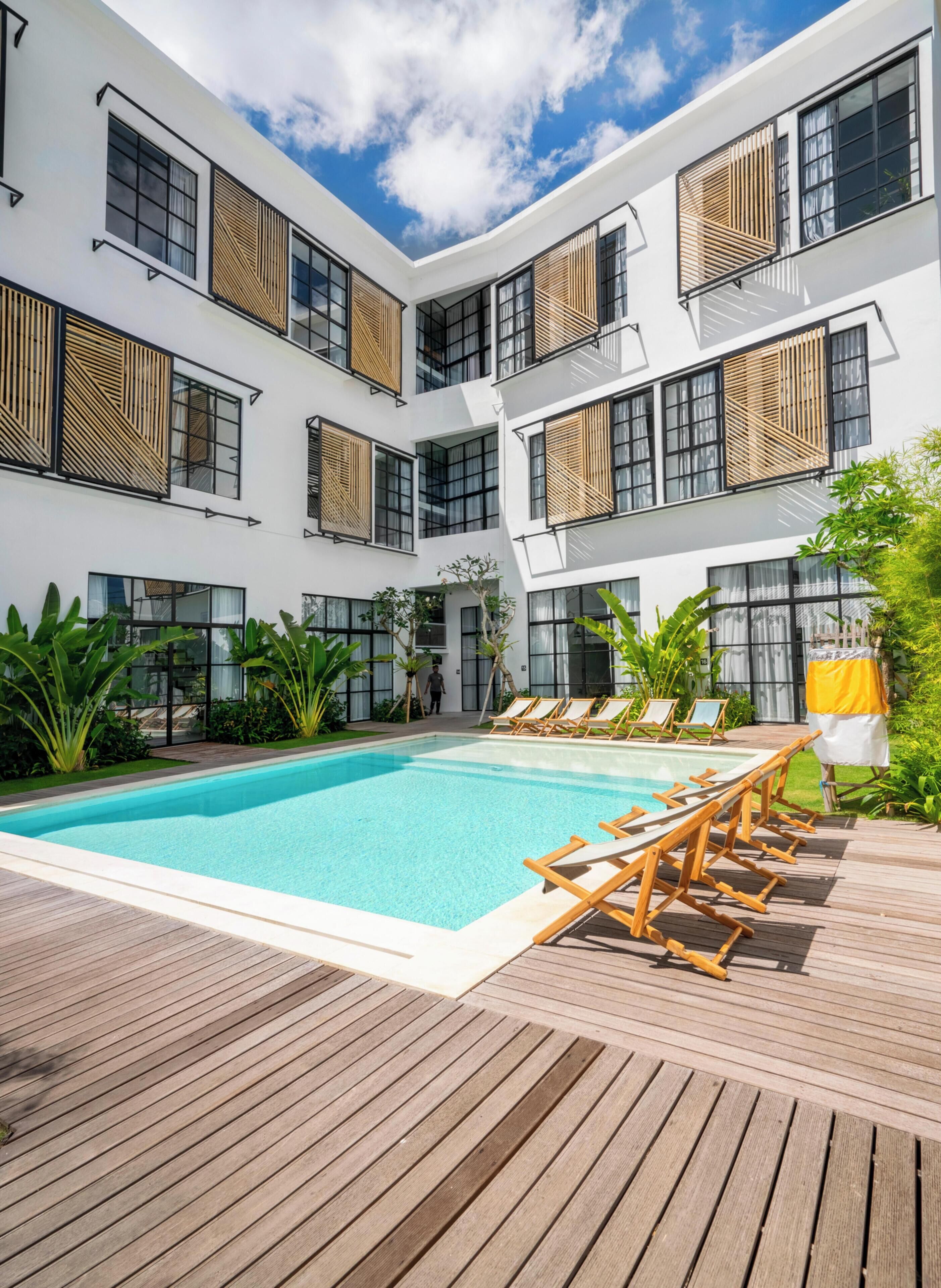 A modern hotel with a pool, wooden deck, and multiple balconies with wooden slats.