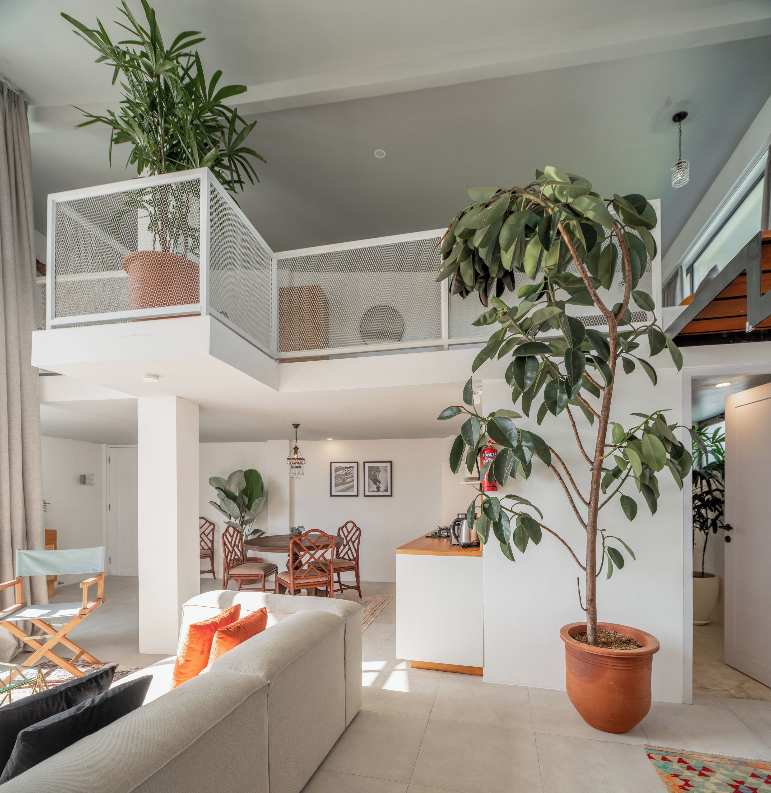 A spacious living area with a high ceiling, a dining table with chairs, a sofa, and a potted plant.