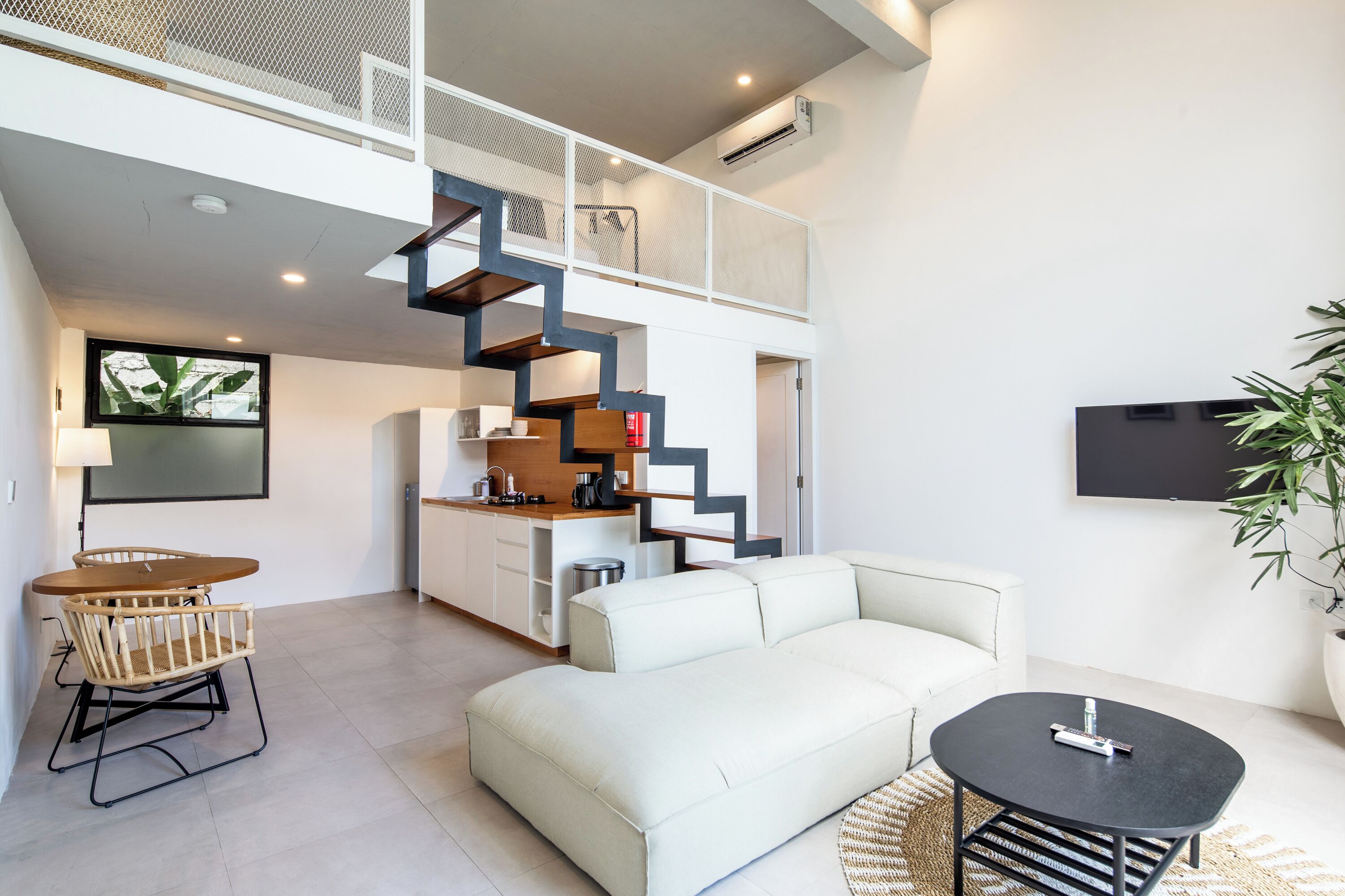 Ein moderner Wohnraum mit einem weißen Sofa, einem Esstisch mit Stühlen, einer Treppe und einer Küchenzeile.