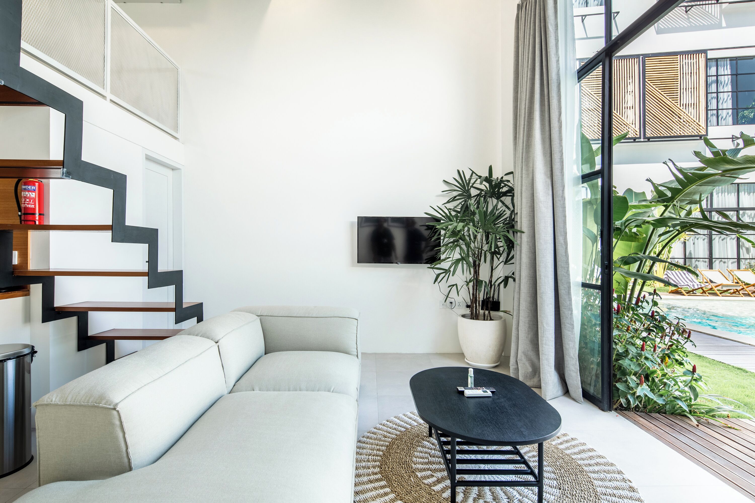 Una sala de estar moderna con un sofá, una mesa de centro, un televisor y un amplio ventanal con vistas a una piscina.
