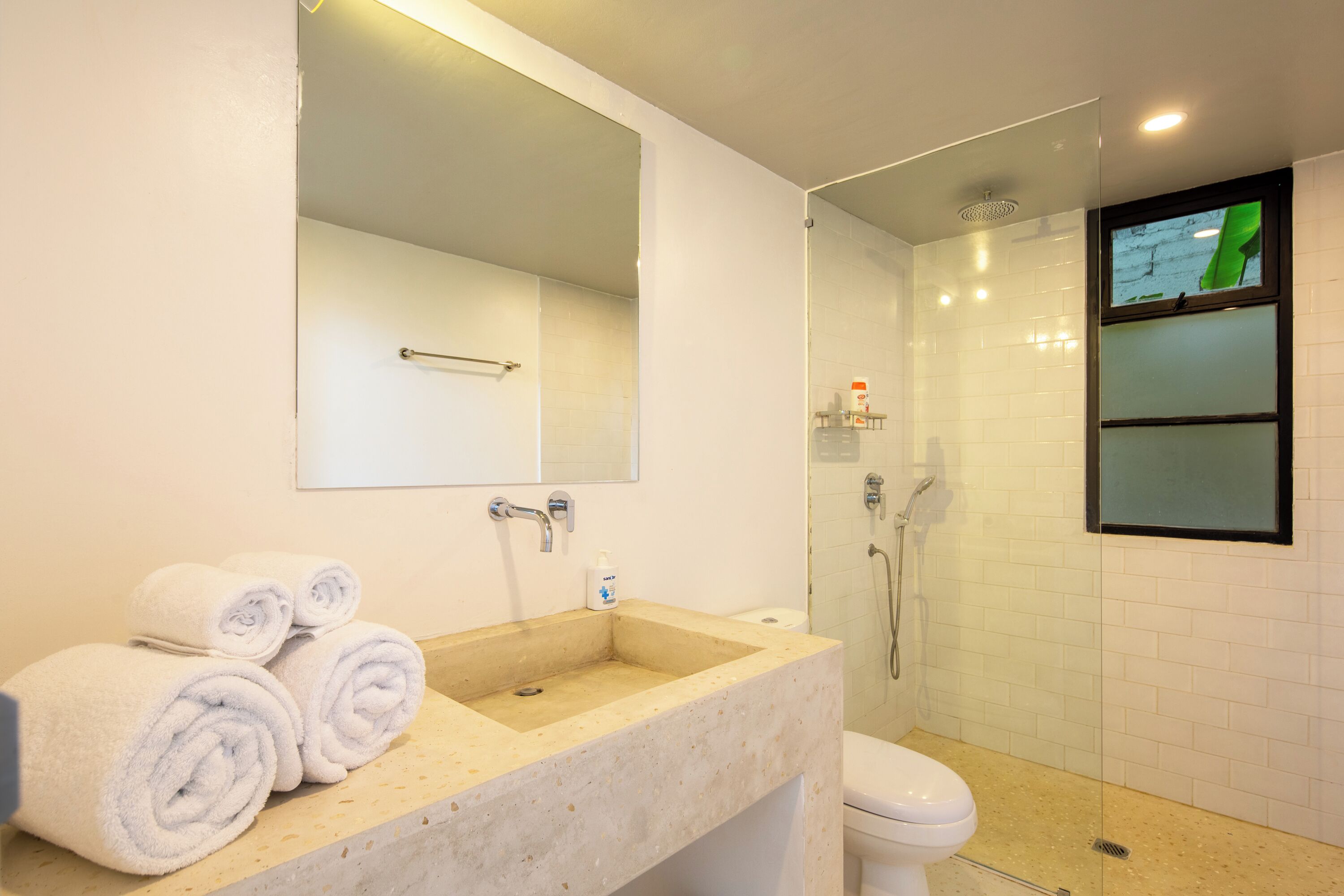 Un baño con un lavamanos color crema, inodoro blanco y ducha con mampara de vidrio.