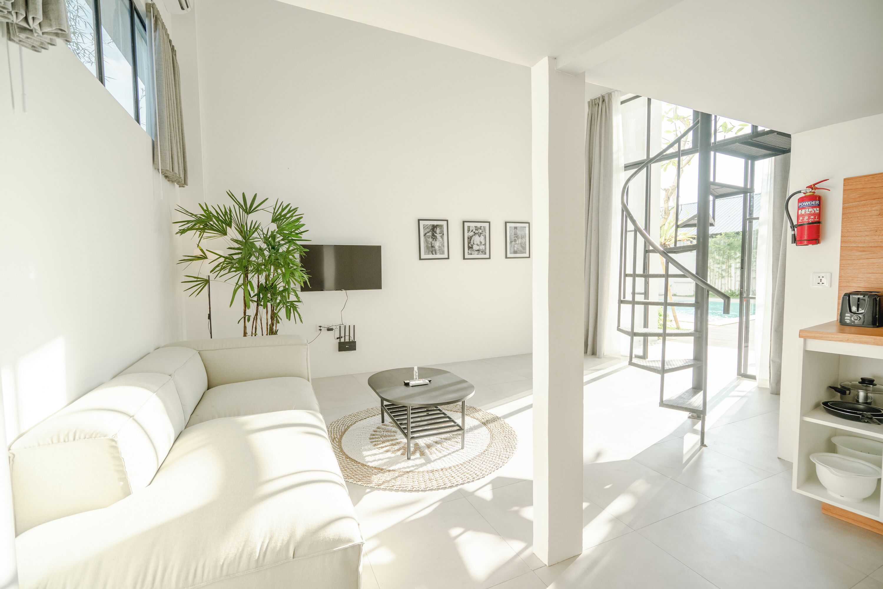 Una sala de estar moderna con un sofá blanco, una mesa de centro, un televisor y una escalera que da a un espacio exterior.