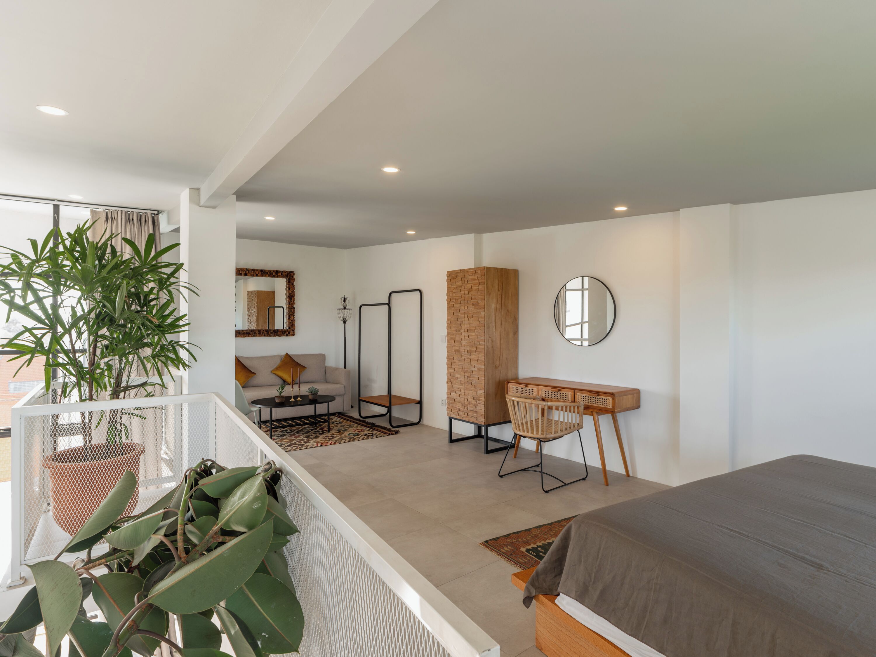 A modern bedroom with a bed, a seating area with a sofa and chairs, a large mirror, and a potted plant.