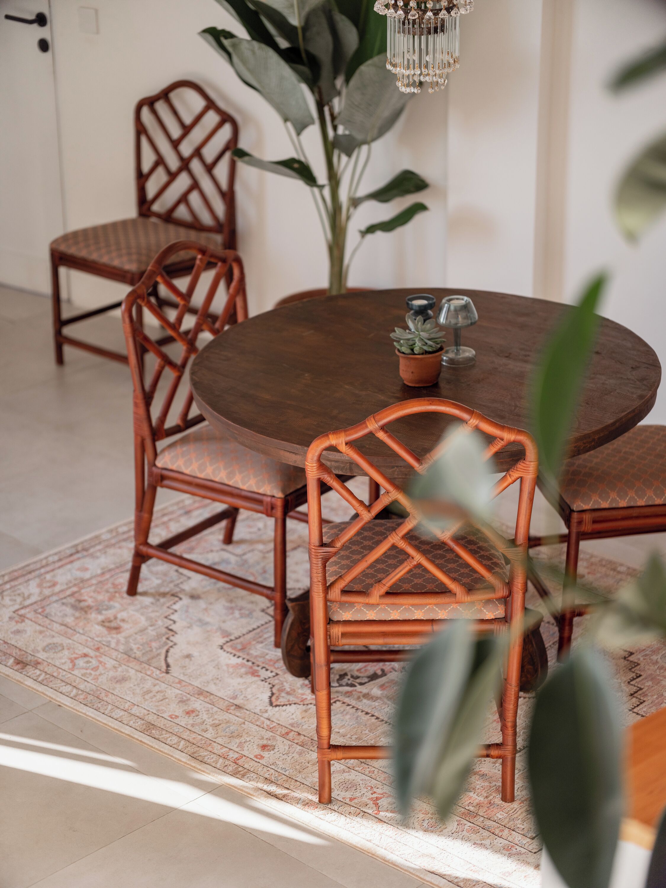 A round wooden dining table with four chairs, a potted plant, and a chandelier.