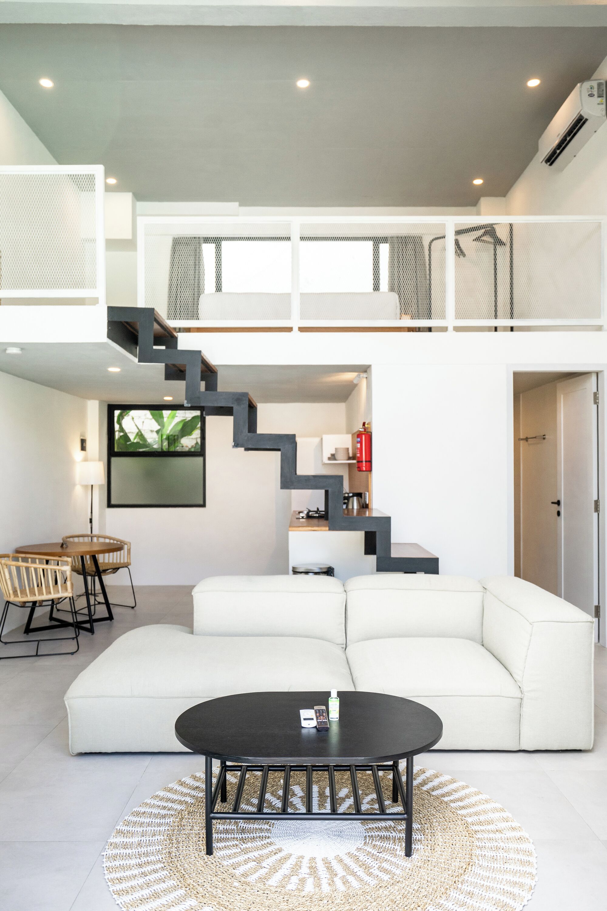 Una sala de estar moderna con un sofá blanco, una mesa de centro negra y una escalera que sube a un nivel superior.