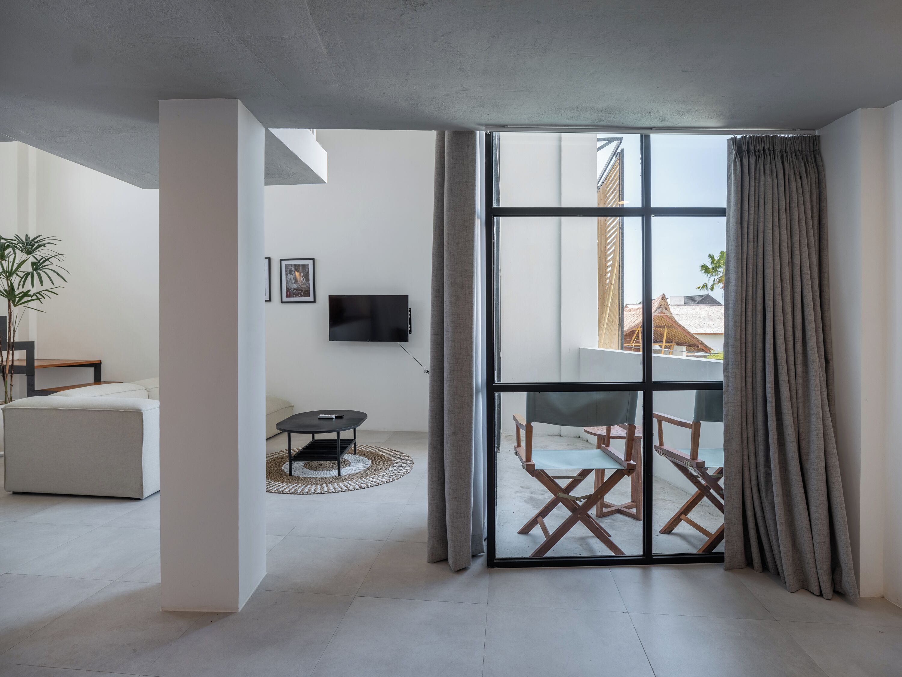A modern living room with a flat-screen TV, a sofa, a small table, and a view through a glass door to an outdoor area with wooden furniture.