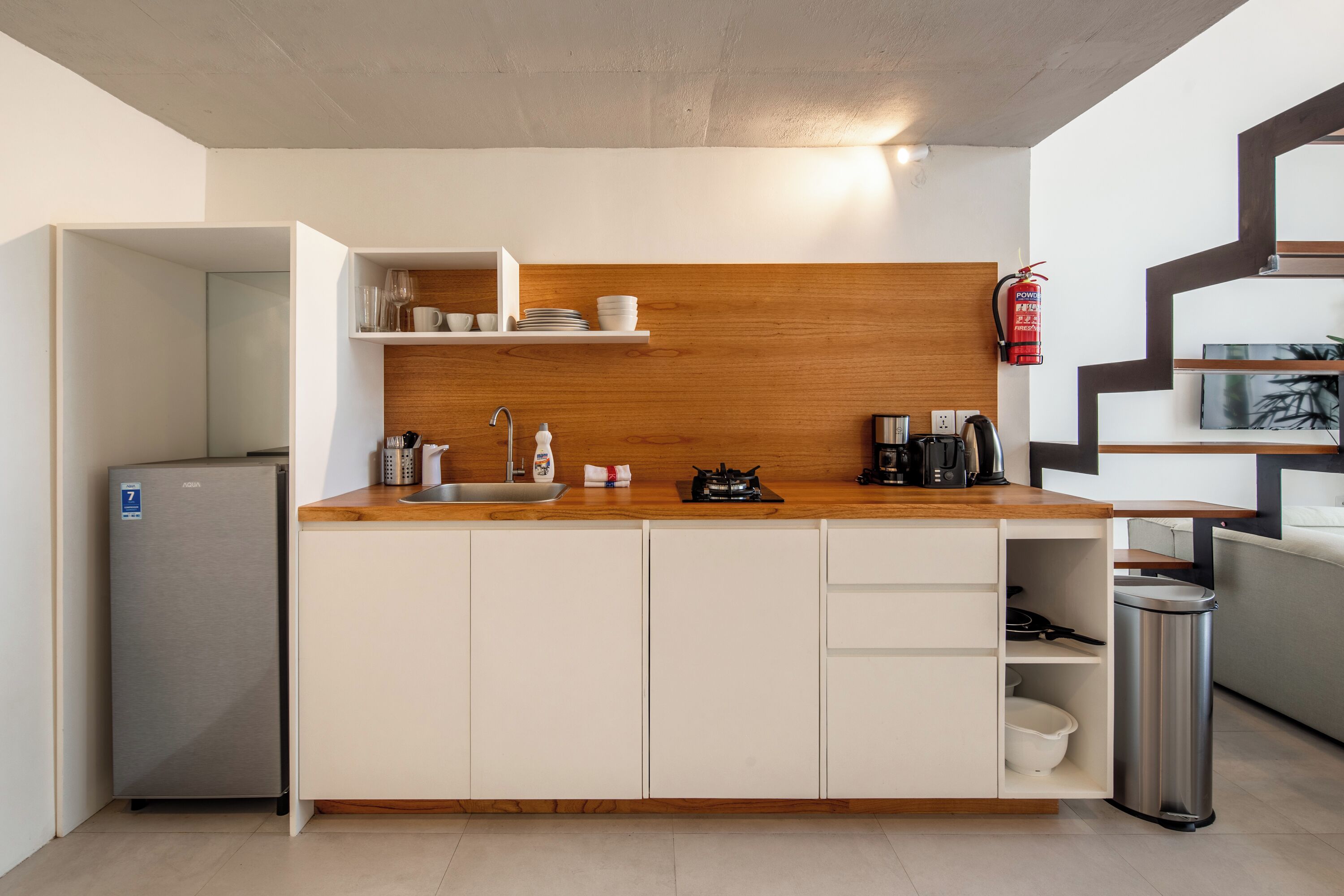 Una cucina moderna con mobili bianchi, un piano di lavoro in legno, un lavello incassato e un cestino in acciaio inossidabile.