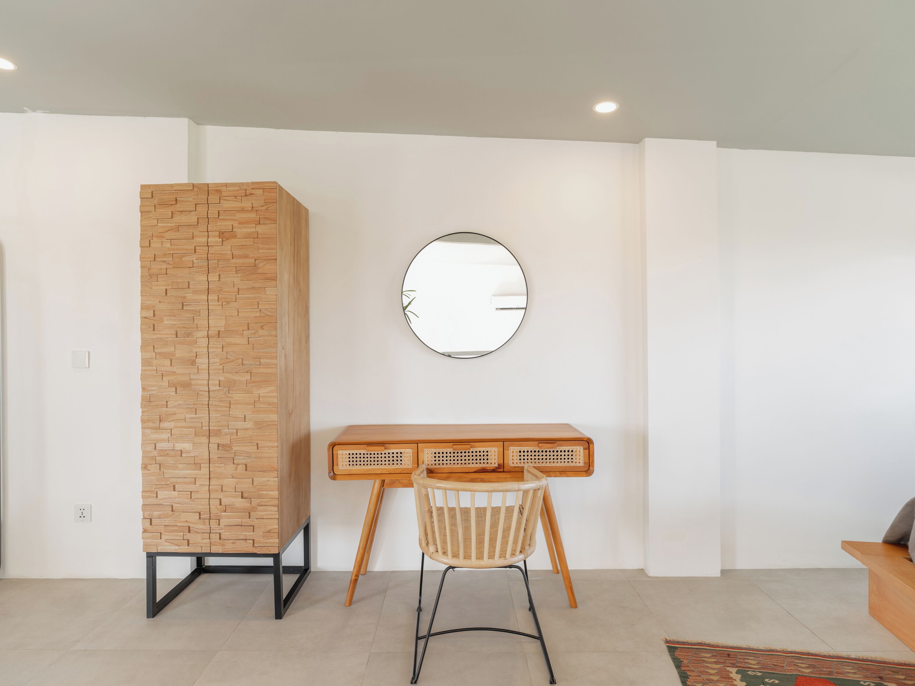 A modern room with a wooden accent wall, a round mirror, a desk with a woven chair, and a small sofa.
