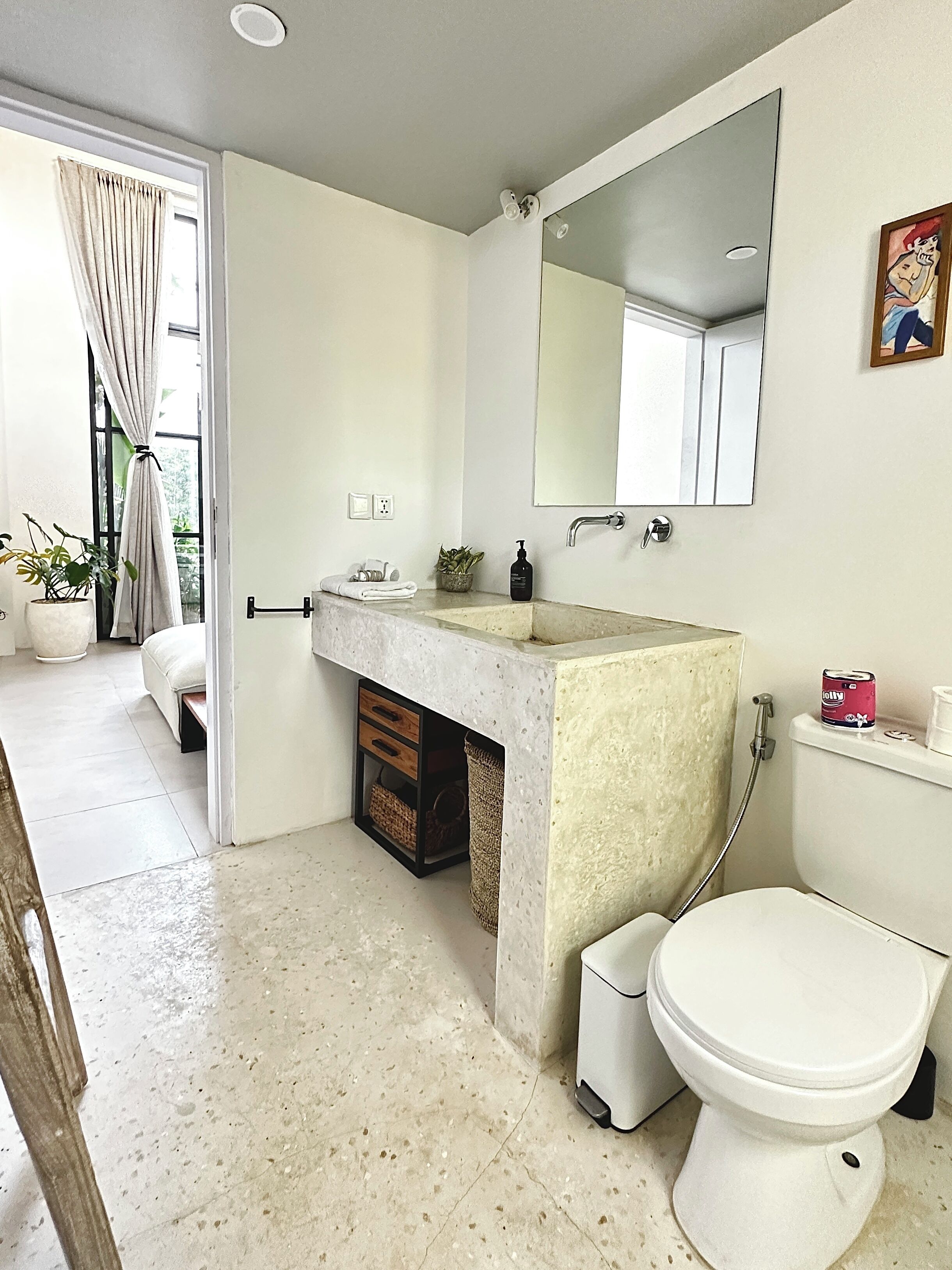A bathroom with a toilet, sink, and shower. There is a mirror above the sink, a potted plant, and a towel rack.