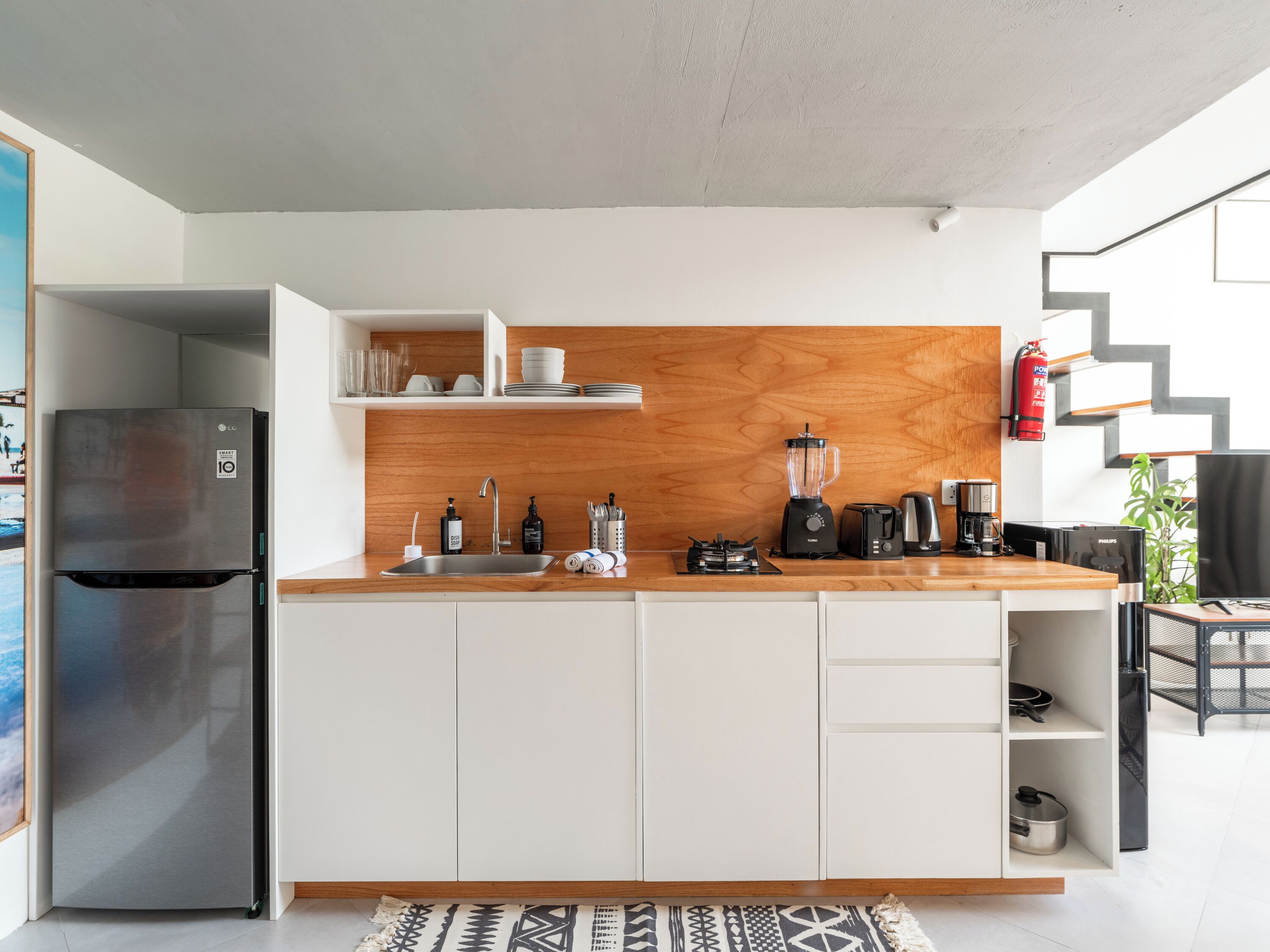 A modern kitchen with white cabinets, a wooden backsplash, a stainless steel refrigerator, a blender, and a coffee maker.