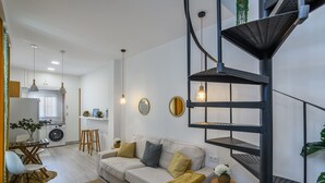 A modern living room with a sofa, a coffee table, and a dining area. There is a kitchen in the background with a washing machine and a sink. - Estudio del Astillero - Ayamonte Centre AEHASP00 (Ayamonte)