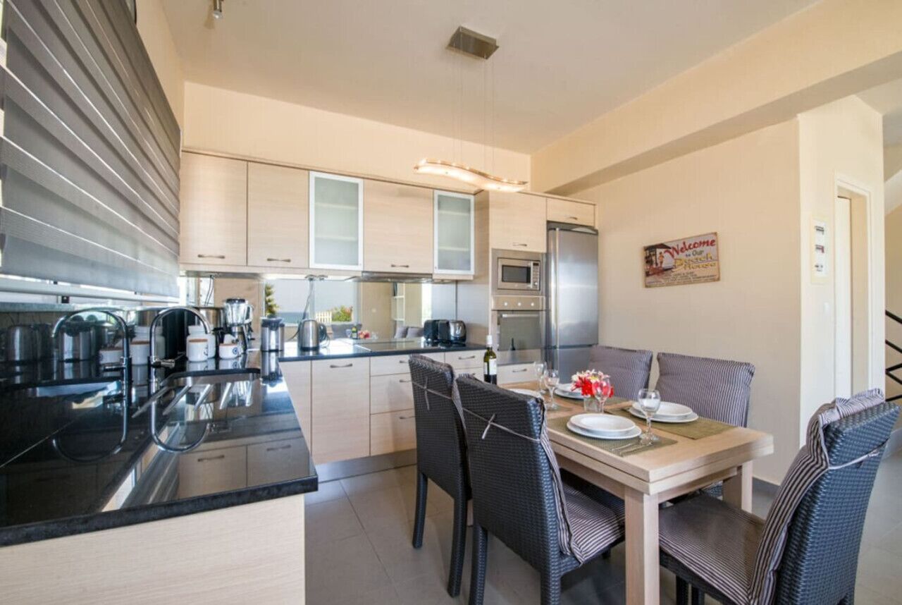 A modern kitchen with a dining area, featuring a central island, built-in appliances, and a welcoming sign.