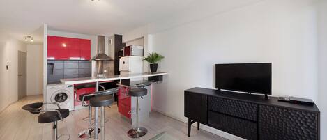 Una cocina moderna con armarios rojos, un televisor negro sobre un mueble, y una zona de bar con taburetes.