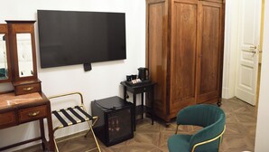 A room with a flat-screen TV, a wooden wardrobe, a small black cabinet, a green chair, and a wooden desk with drawers. - LN B&B (Catania)