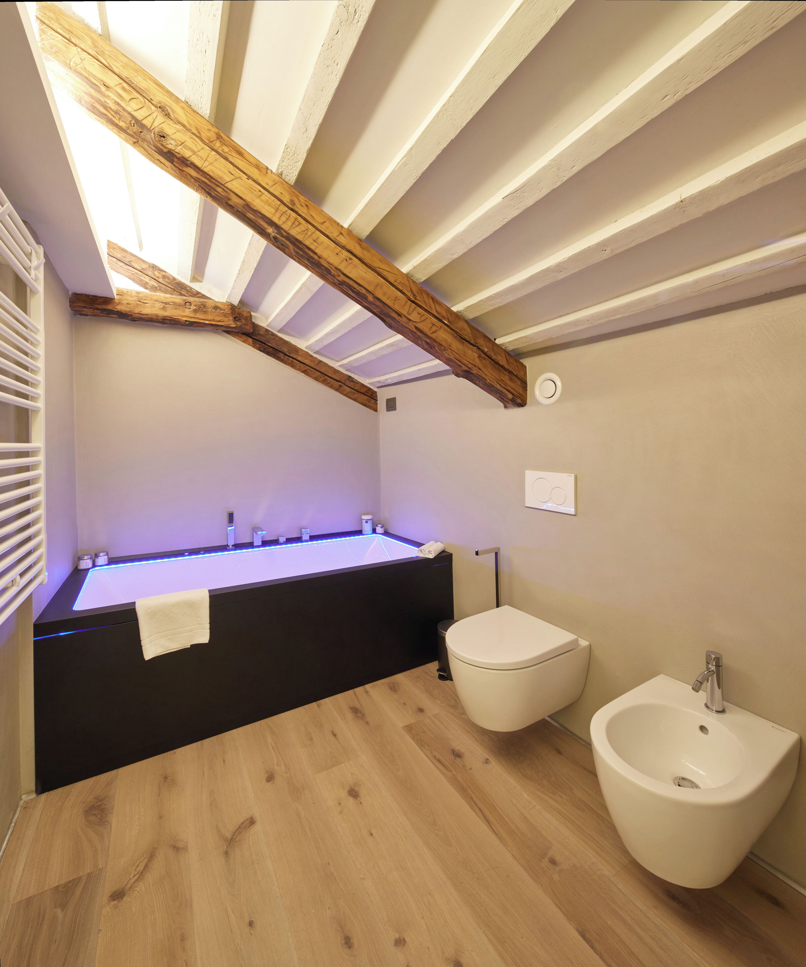 A modern bathroom with a wooden ceiling, a black vanity, two white bidets, and a wooden floor.