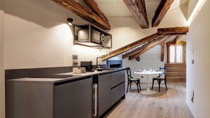 A modern kitchen with dark cabinetry, a central island, and exposed wooden beams. - Palazzina Riva (Venice)