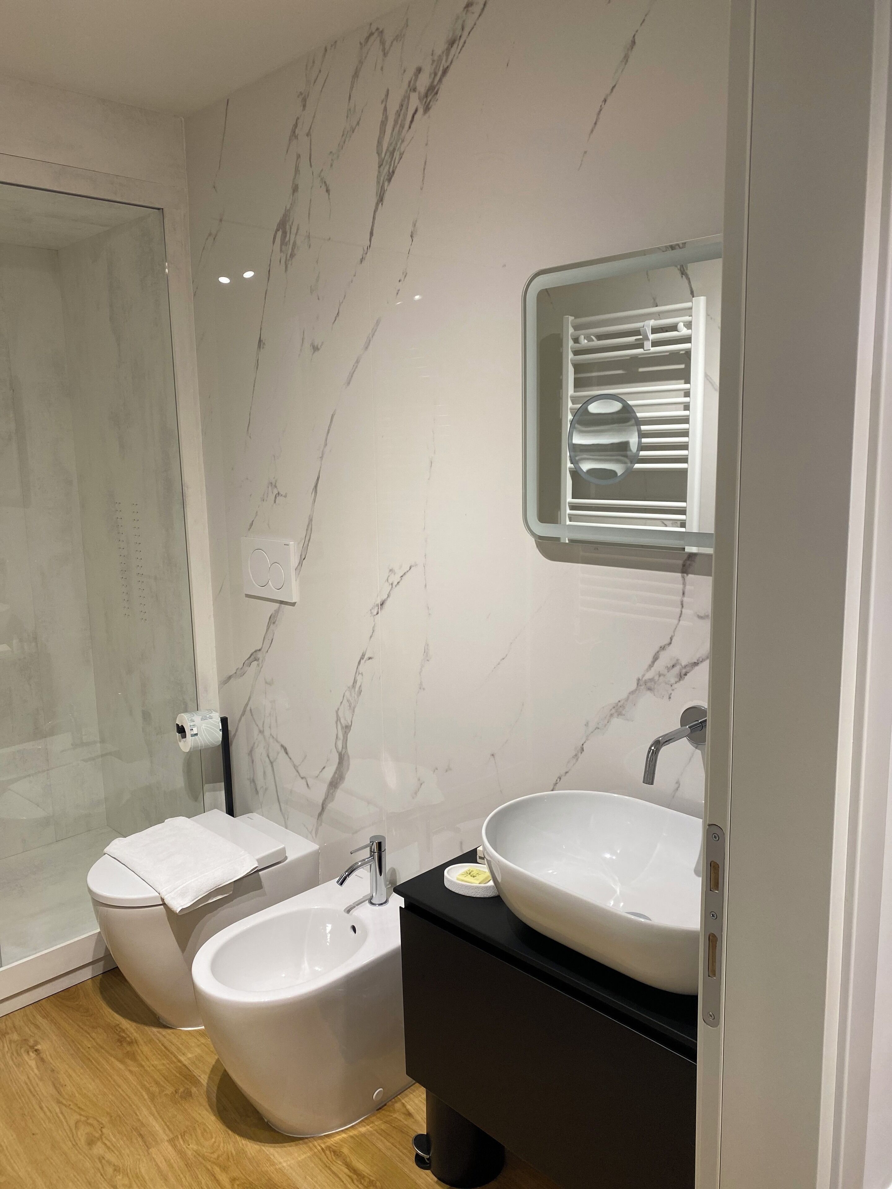 Un bagno moderno con una parete in marmo, box doccia in vetro, un water, un bidet e un mobile lavabo.
