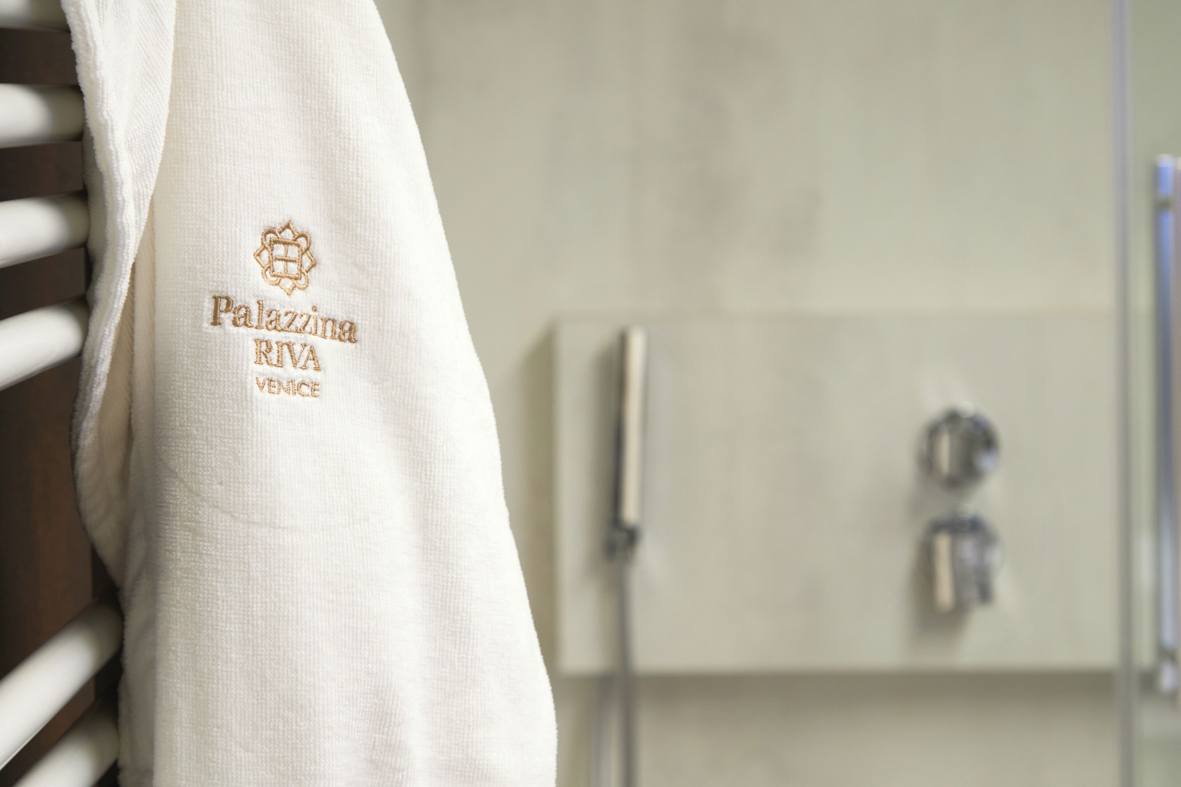 A white towel with embroidered text "Palazzina Riva Venice" hanging on a rack.