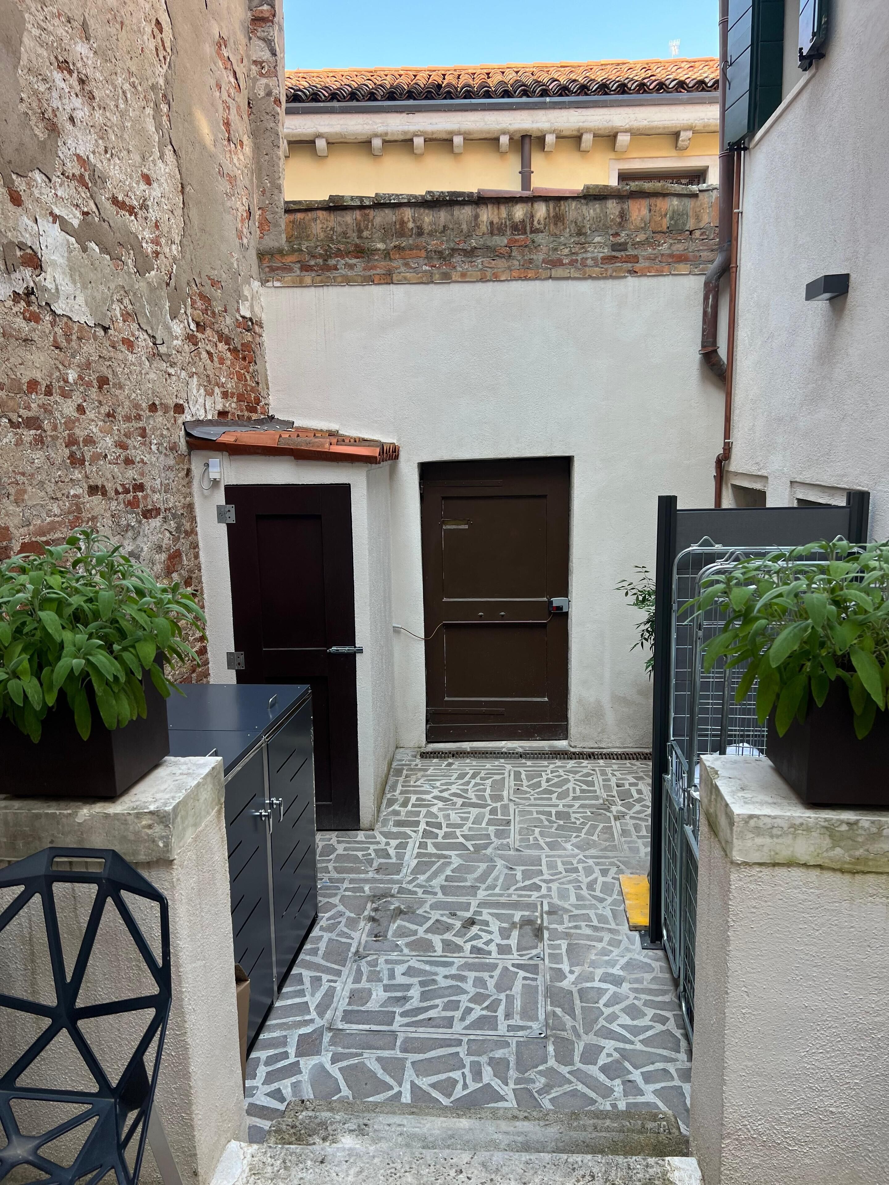 Un cortile stretto con pavimento piastrellato, due porte e piante in vaso.