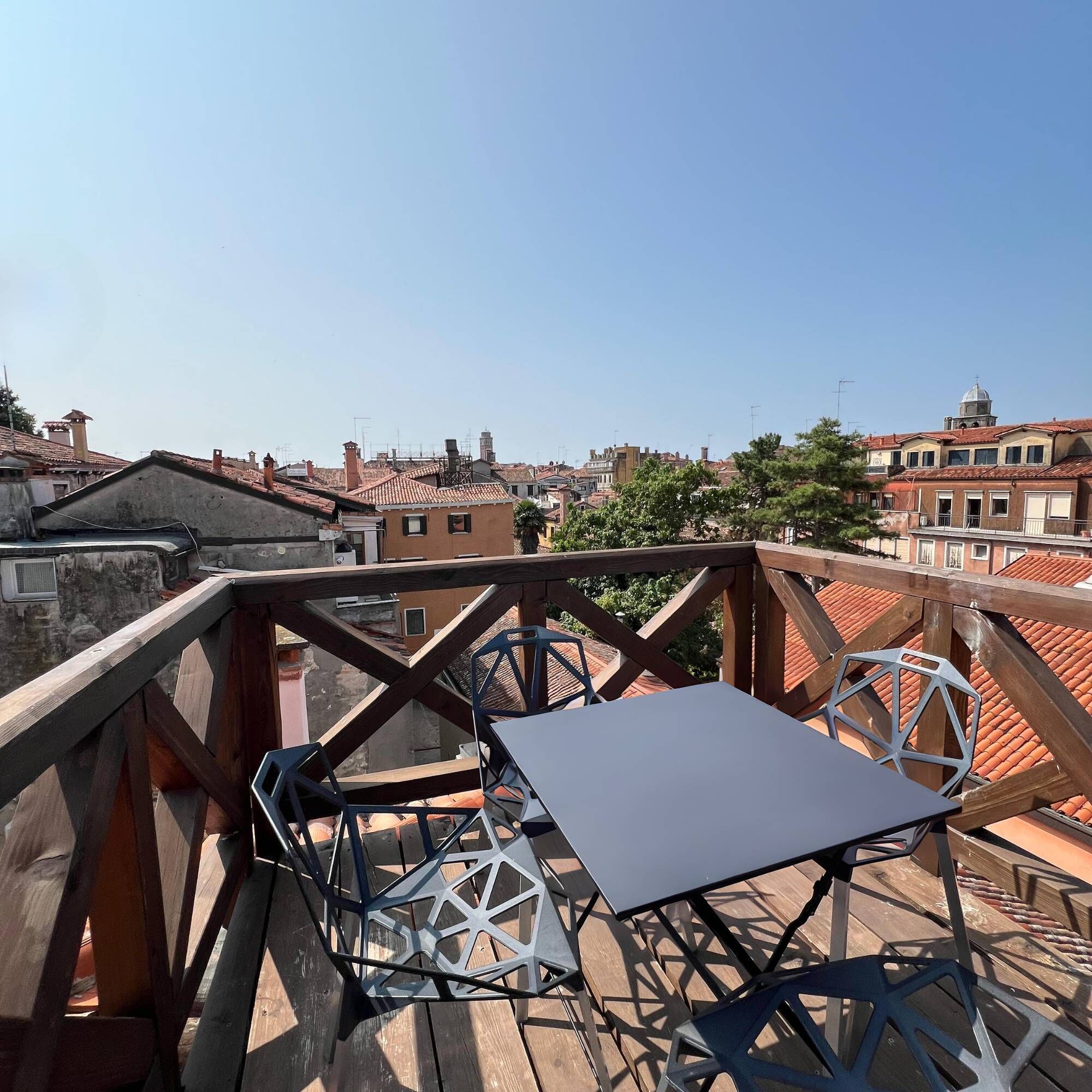 A rooftop terrace with a table and chairs, offering a view of the cityscape.