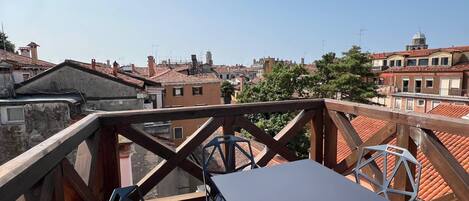 A rooftop terrace with a table and chairs, offering a view of the cityscape.