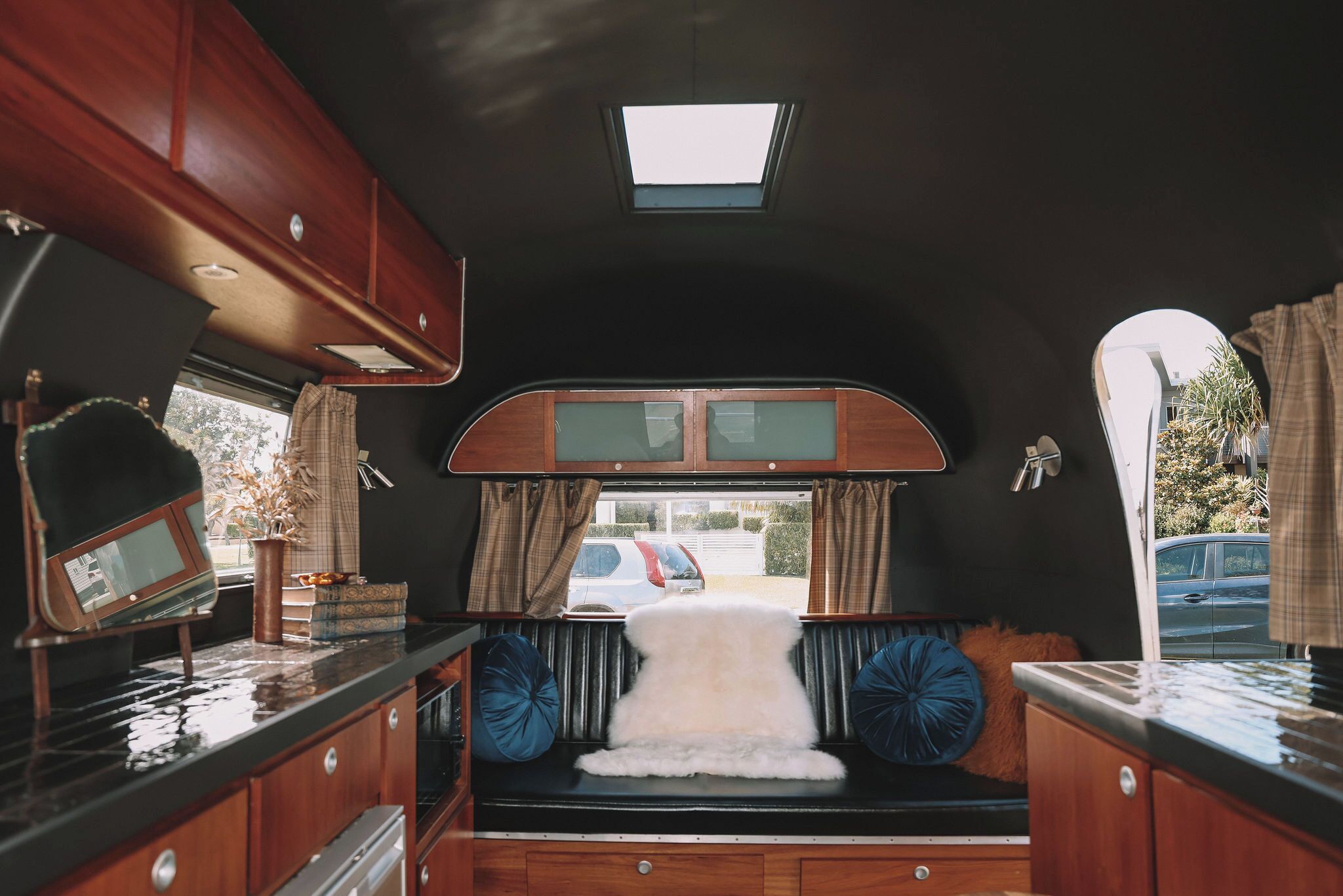 A compact RV interior with a kitchenette, a small seating area with a fur throw, and a window with curtains.