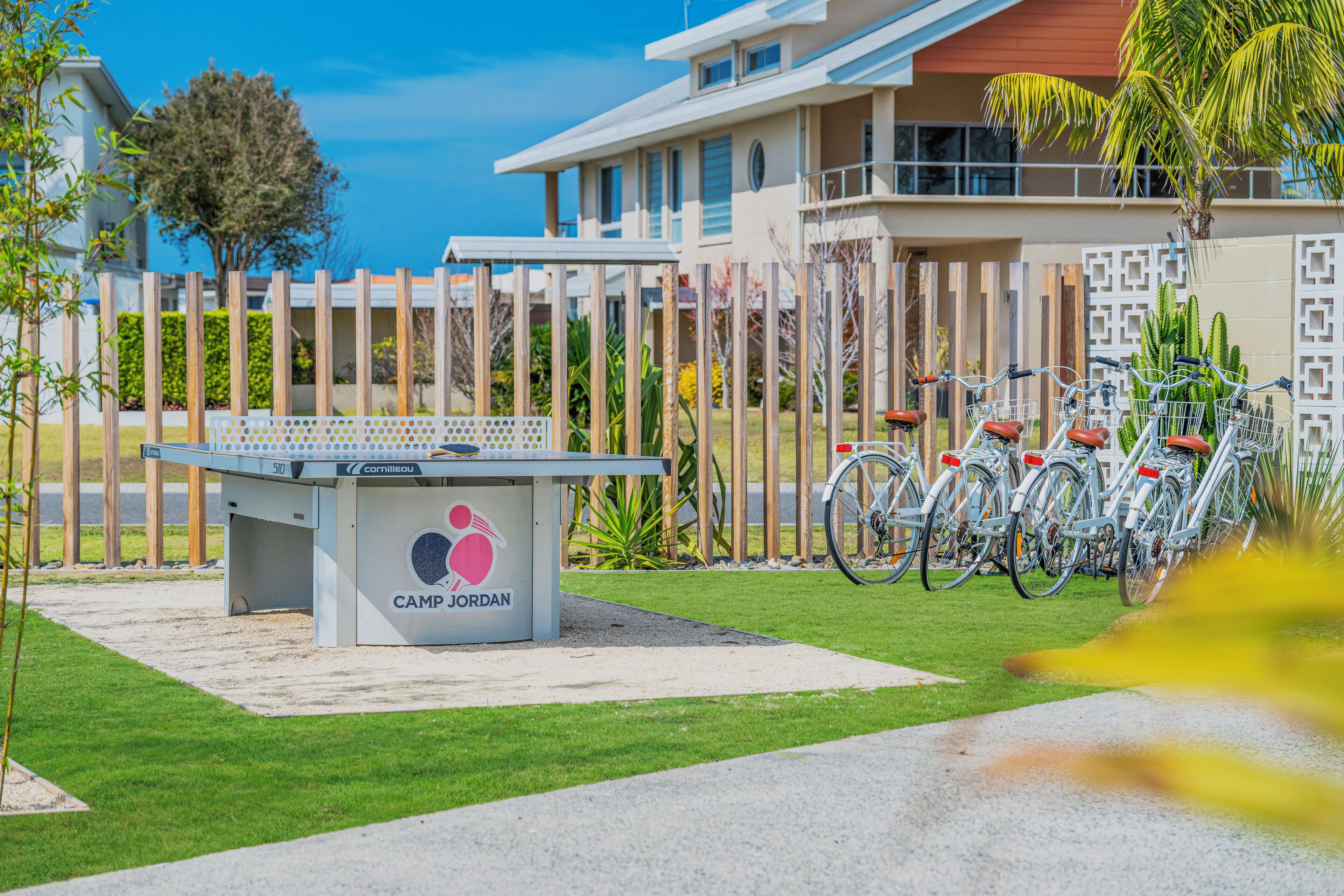 A pool table with a "CAMP JORDAN" logo, surrounded by a fenced area with bicycles parked nearby.