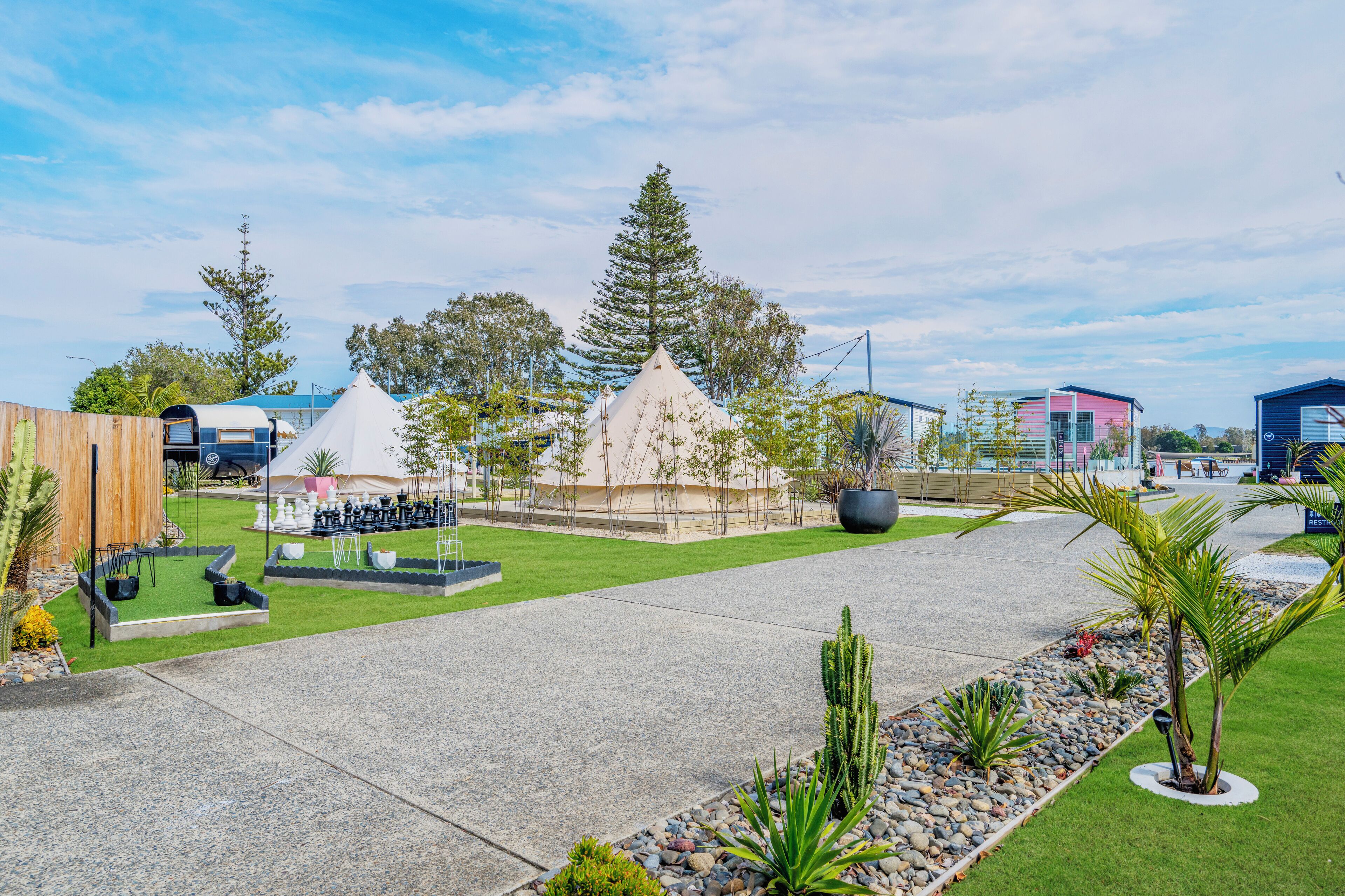 A courtyard with a grassy area, a white tent, a conical structure, and a pink building.