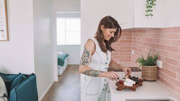 A person preparing food in a kitchen with a brick backsplash, a hanging plant, and a view of a bedroom in the background.