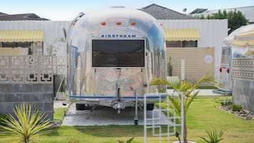 A vintage Airstream trailer with a 'Birt' logo, surrounded by a landscaped garden with palm plants and a decorative fence.
