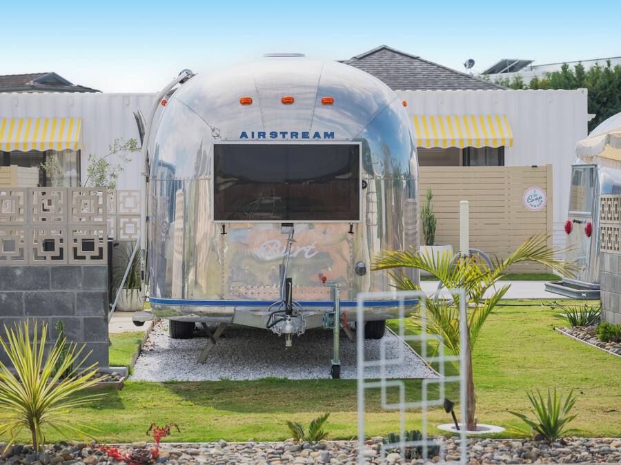 A vintage Airstream trailer with a 'Birt' logo, surrounded by a landscaped garden with palm plants and a decorative fence.