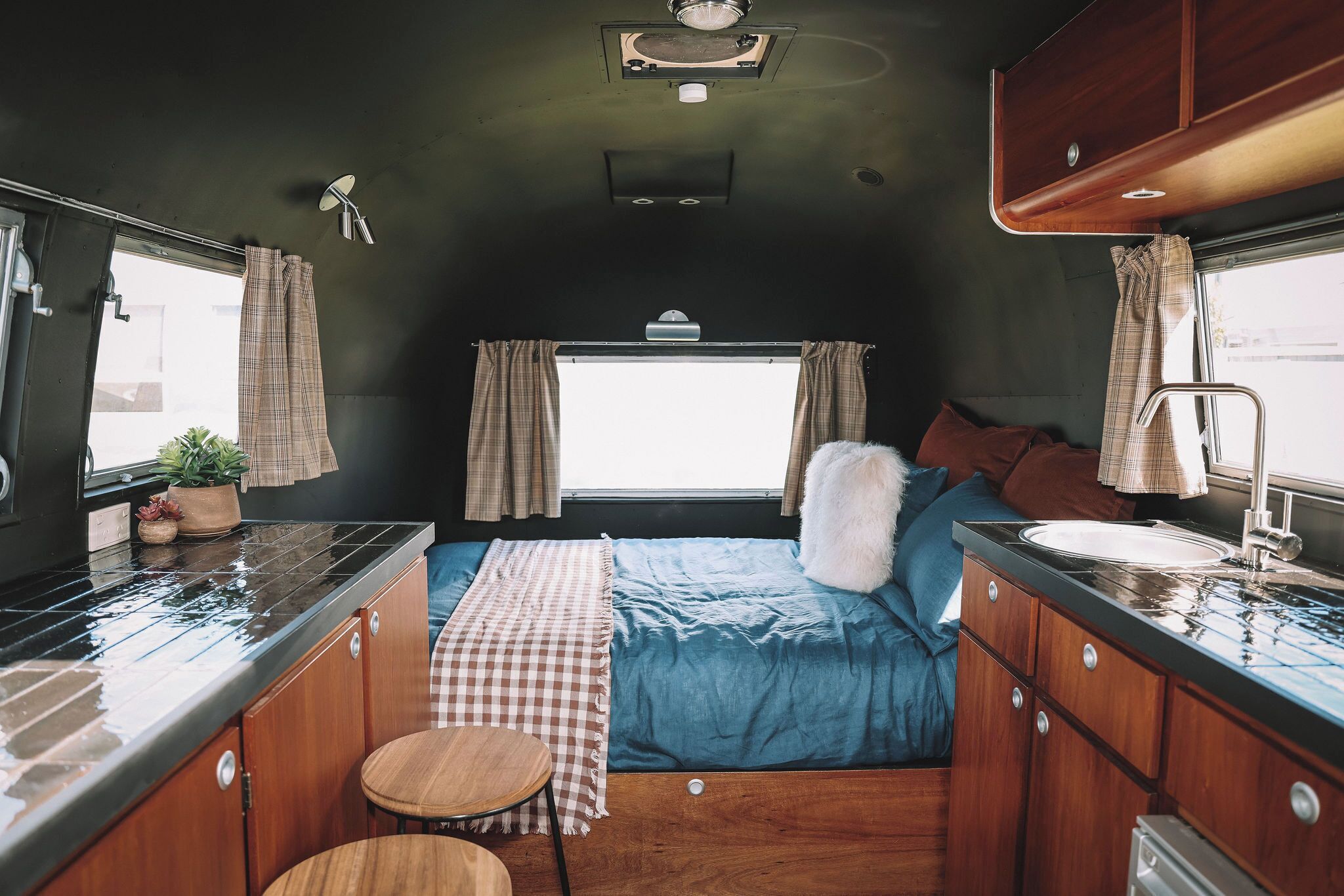 Un intérieur de camping-car compact comprenant un coin cuisine, un lit avec une literie bleue et une fenêtre avec des rideaux.