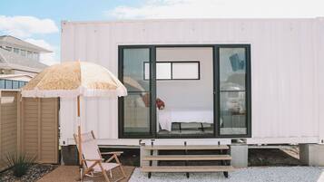 Une maison conteneur moderne dotée d’une grande fenêtre, d’un banc et d’un parasol.