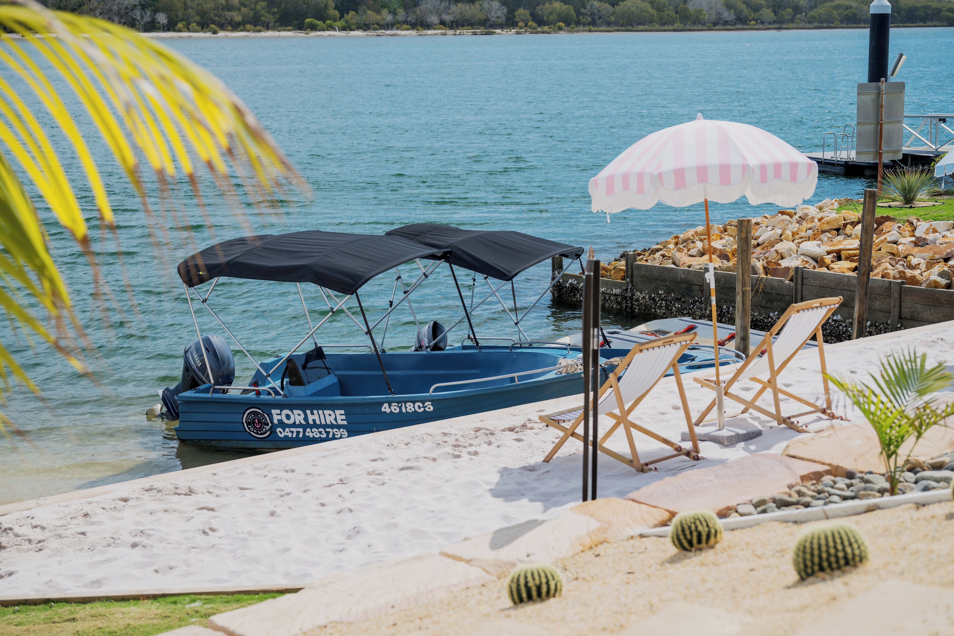 Ein Boot liegt an einem Sandstrand, in der Nähe befinden sich eine Liege und ein Sonnenschirm.