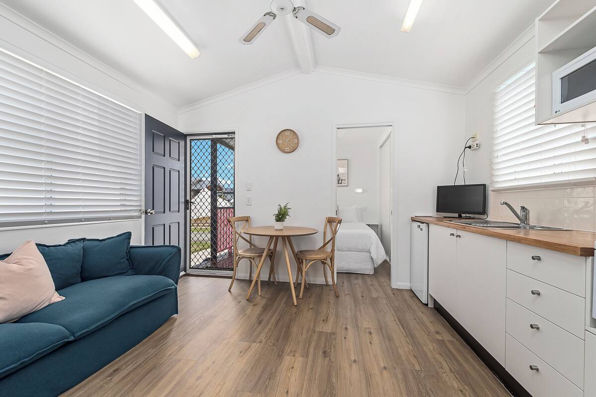 Un espacio habitable compacto con sofá, mesa de comedor, sillas, televisor y zona de cocina.