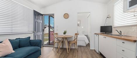 A compact living space with a sofa, dining table, chairs, a TV, and a kitchen area.