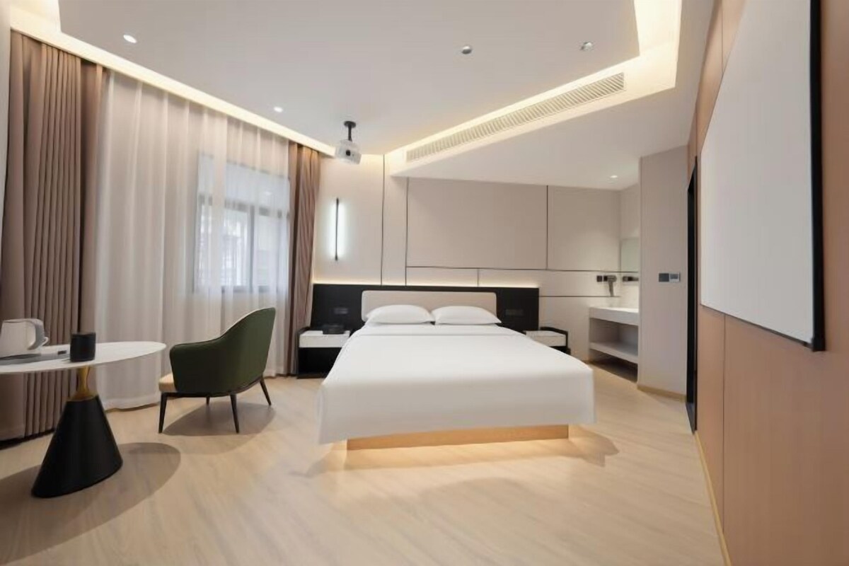 A modern hotel room with a bed, bedside table, chair, and a desk with a chair.