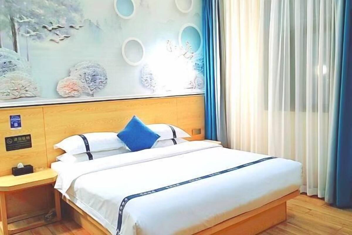 Una cama bien hecha con ropa blanca y una almohada azul, un cabecero de madera y una mesita de noche con una caja de pañuelos.