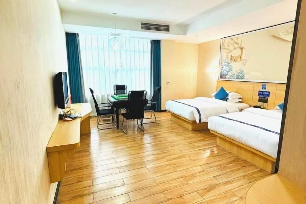 Habitación de hotel con dos camas, un escritorio con silla, televisión y un espejo grande.