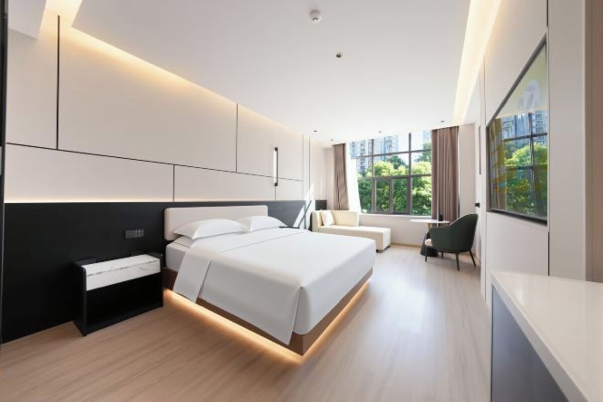 A modern bedroom with a large bed, bedside tables, a desk, and a window with a view.