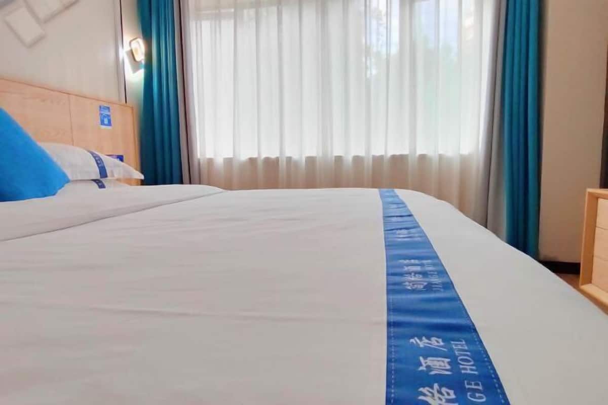 Una habitación de hotel con cama, cortinas y un cartel visible sobre la colcha.