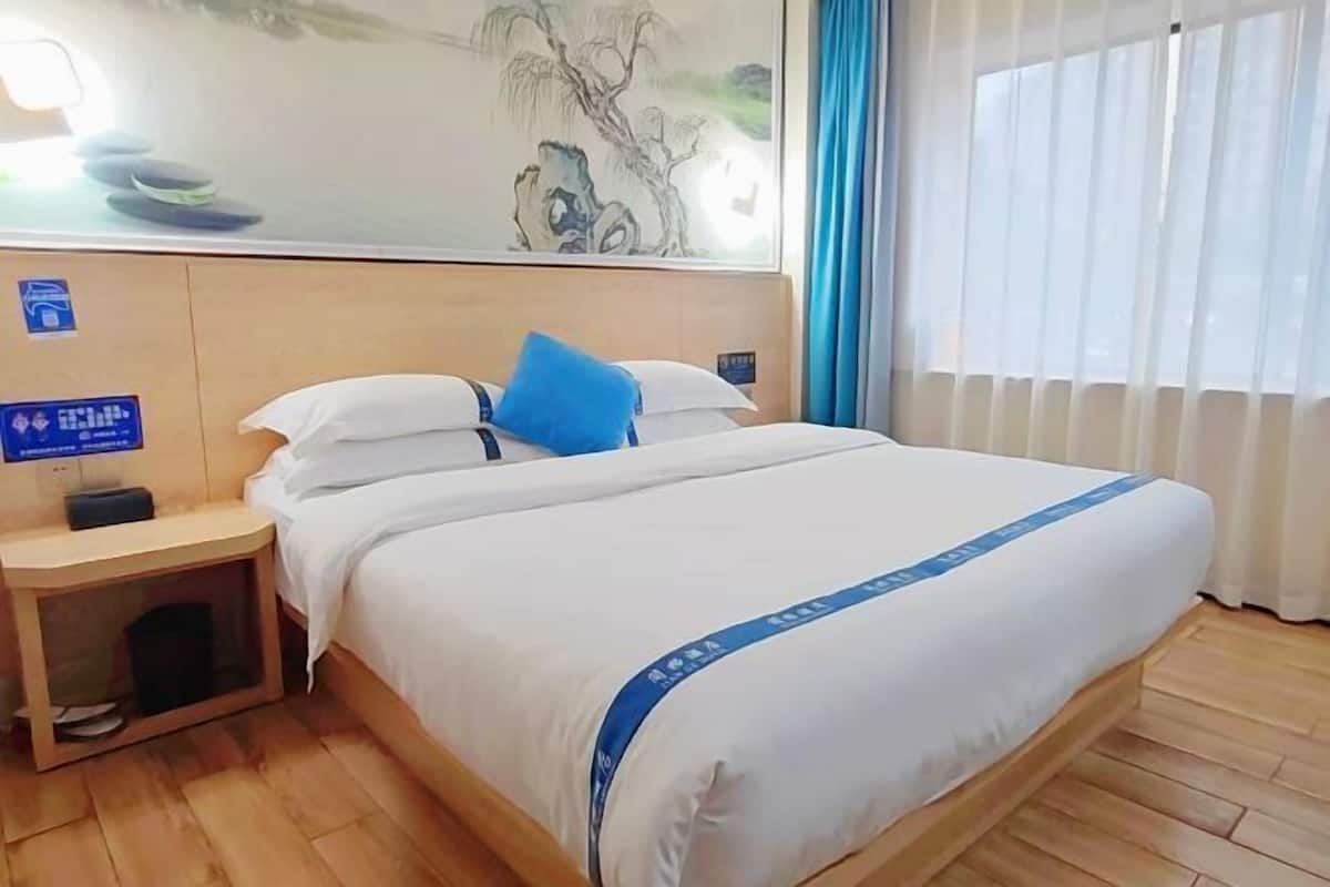 Una habitación de hotel con una cama, una mesita de noche, una obra de arte colgada en la pared y una ventana con cortinas.
