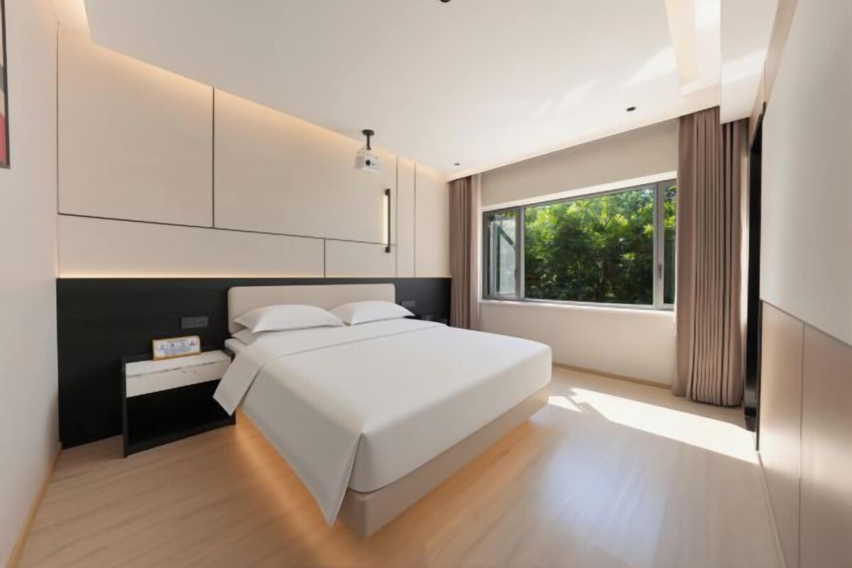A modern bedroom with a large bed, a nightstand, and a window with curtains.