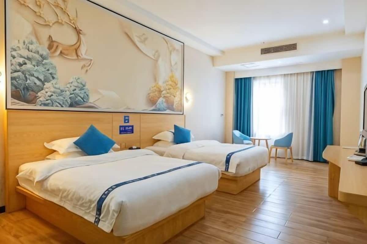 Habitación de hotel con dos camas, un escritorio, una silla y un mural grande en la pared.