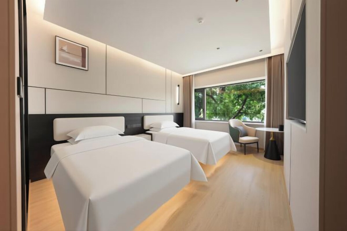 A modern hotel room with two beds, a desk, and a large window.
