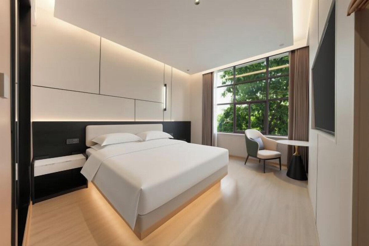 A modern hotel room with a large bed, bedside table, and a desk with a chair.