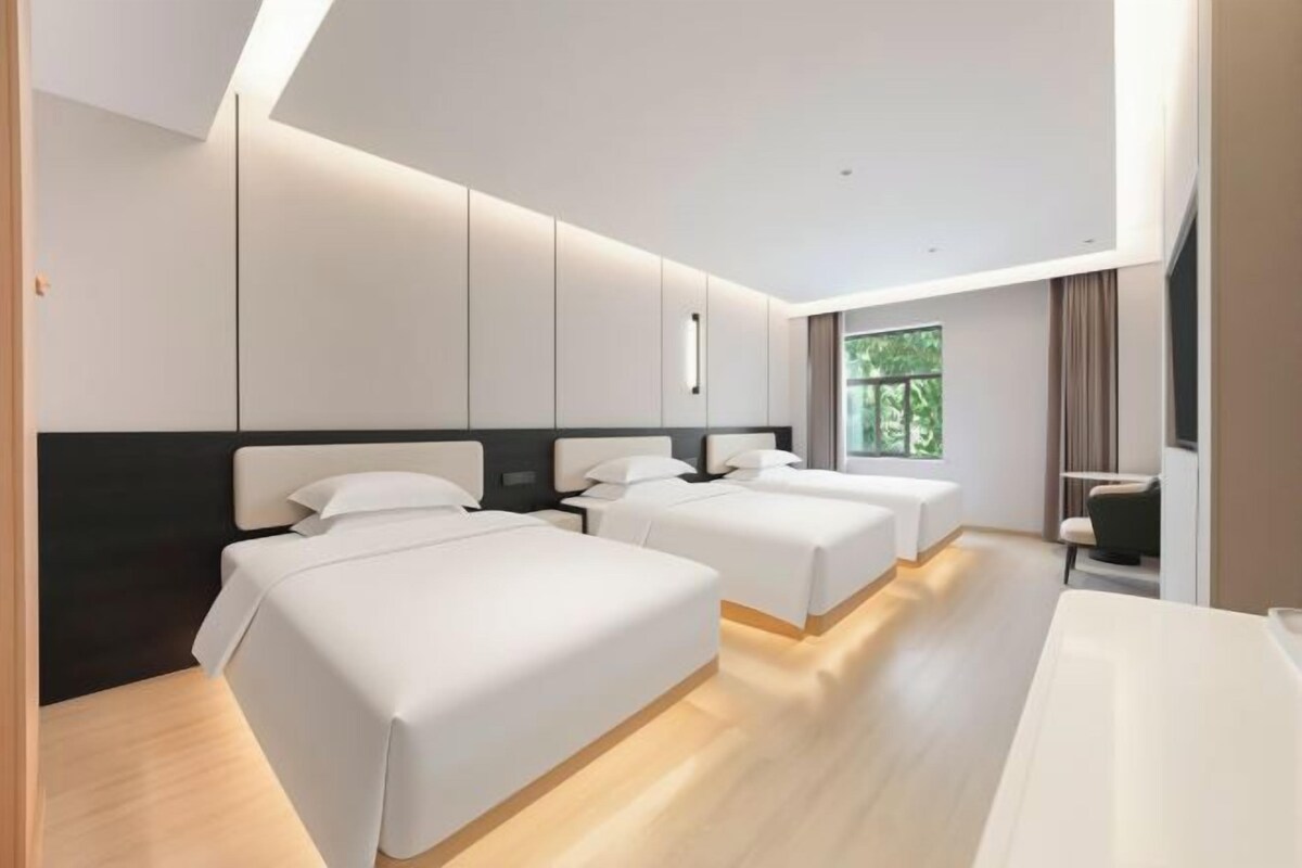 A hotel room with two beds, a desk, and a window with a view of greenery.