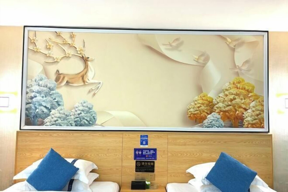 A hotel room with a large wall mural, a wooden headboard, and two beds with blue pillows.